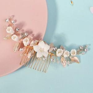 Dettaglio di fiori in ceramica bianca e foglie dorate su un pettine per capelli da sposa