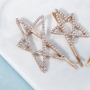 Detalle de dos pinzas para el cabello doradas con estrellas de diamantes sobre mármol
