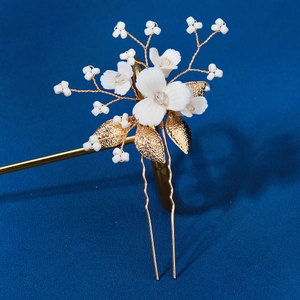 Détail d'épingle à cheveux fleur en céramique blanche et feuilles dorées pour mariée