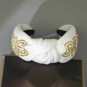 Detail eines weißen Knotenstirnbandes mit handgenähtem BRIDE-Schriftzug aus Goldperlen