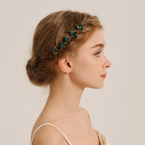 Elegant gold bridal hair pin with green rhinestones in leaf design on bride's hair