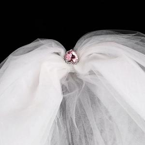 Gros plan d'une pierre rose en cœur et strass argentés sur un voile de mariée blanc