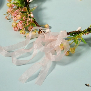 Detail of pink floral wreath headband with sheer organza ribbons on a light blue surface