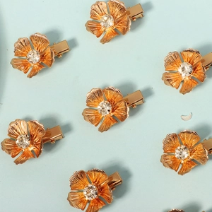 Golden metal flower hair clips with crystal centers arranged on a light blue background