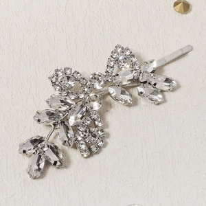 Elegant silver leaf hair clip with crystal rhinestones on a beige textured background