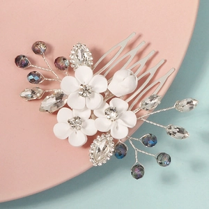 Close-up of white clay flowers and crystal beads on a bridal silver hair comb