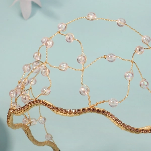 Macro d'un serre-tête de mariée en fil doré tissé avec perles roses irisées et strass brillants