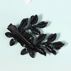 Detail einer schwarzen Metall-Haarspange mit Blättern und Perlen auf blauem Grund