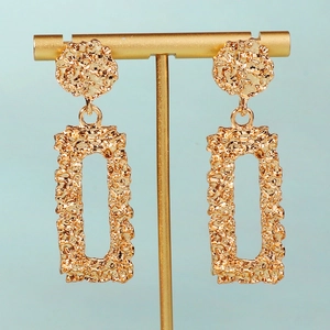 Boucles d'oreilles pendantes rectangulaires dorées texturées sur un porte-bijoux