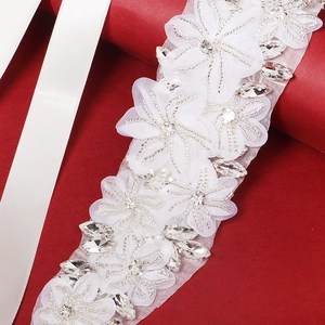 Détail de ceinture de mariée avec fleurs en résille blanche, strass et perles d'argent