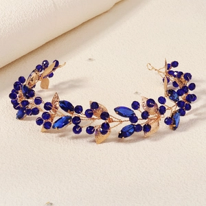 Détail de branches dorées avec cristaux bleu roi et feuilles mates sur un peigne de mariée