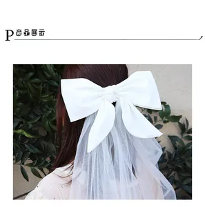 Detail view of a white satin bow hairclip with long bridal veil on a woman's hair