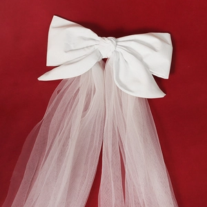 Elegant white satin bow hair clip with long tulle bridal veil on a textured red surface