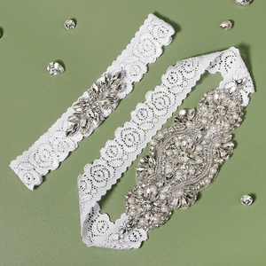 Elegant bridal lace garter set with rhinestone flower and pearl accents on green background