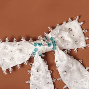 Détail macro du nœud en satin blanc avec cristaux bleus et paillettes cousus à la main