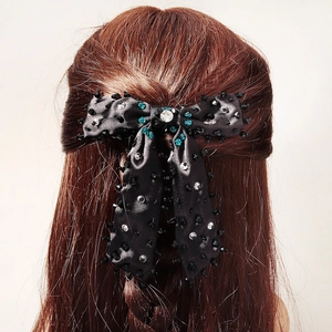 Détail d'une pince à cheveux avec nœud en satin noir ornée de perles et de strass brillants