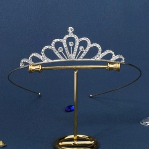 Silver bridal crown with clear rhinestones on a wave design shown on a gold jewelry stand