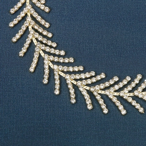 Détail d'un serre-tête doré avec chaîne en épi et strass blancs sur fond bleu foncé
