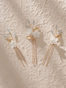 Detail of bridal hair pins with white ceramic flowers, gold leaves and blue crystals