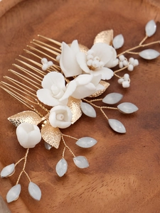 Close-up of white ceramic flower bridal hair comb with gold metal leaves and pearls