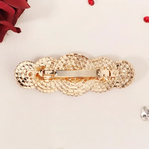 Detail view of a gold spring hair clip with white crystals and red rose background