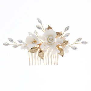 Detailopname van bruidshaarkam met witte keramische bloemen en goudkleurige bladeren