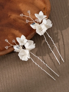 Detail of two white ceramic flower hair pins with crystals and pearls on wood base