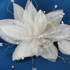 Detail of handmade white mesh flower hairpiece with crystals and pearls on blue background