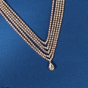 Macro view of a gold-tone layered rhinestone V-necklace with a teardrop crystal pendant