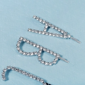 Détail de trois barrettes argentées avec strass en forme de lettre H et de lunettes