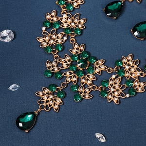 Macro detail of gold flower necklace with emerald green crystals on navy background
