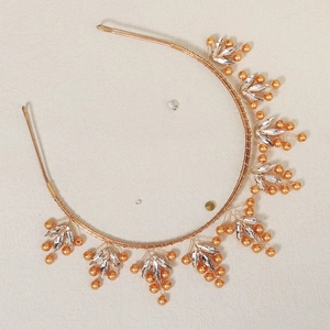 Détail d'un serre-tête doré fait main avec perles et cristaux sur fond clair texturé