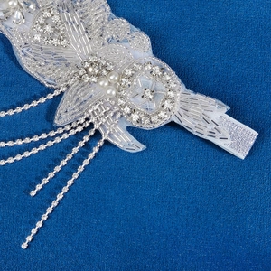 Serre-tête de mariée élégant avec perles à la main, strass et glands sur fond bleu