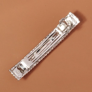 Silver rectangular hair clip with five rows of sparkling rhinestones on brown background