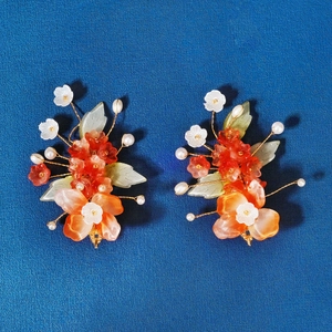 Detailed close-up of handmade red resin flowers with pearls and green jade-like leaves