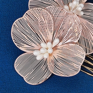 Détail d'un peigne à fleurs en or rose avec pétales en métal ajouré et perles