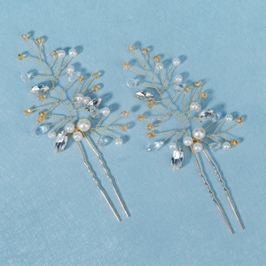 Close-up of golden branch hair pins with white pearls and amber crystals on blue texture