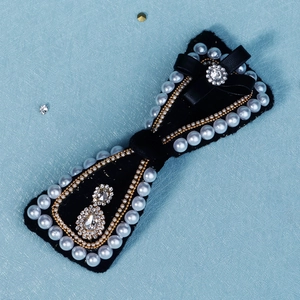 Macro detail of black velvet bow hair clip with pearl edges and sparkling rhinestones