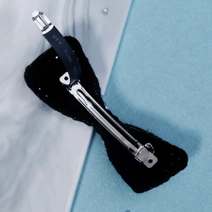 Close-up of the metal spring clip on the back of a black fabric bow hair accessory