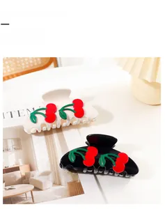 Detail showing two cherry hair claw clips in cream and black with red fruit accents