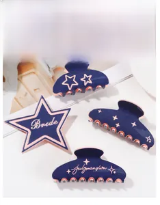 Detail showing four assorted navy blue hair claw clips with star patterns and lettering