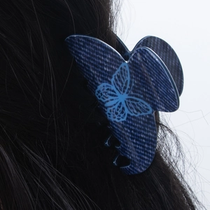 Pince à cheveux papillon texture denim bleu de 7cm présentée sur des cheveux noirs