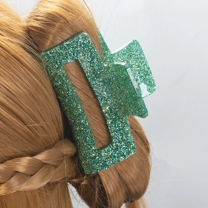 Pince à cheveux rectangulaire vert pailleté portée sur des cheveux blonds avec paillettes