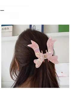 Detail view of a pink iridescent hair claw clip in a bow shape worn on model hair
