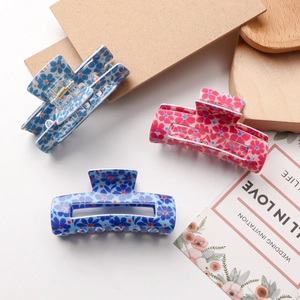 Three floral print claw clips in light blue, dark blue, and pink on a wooden tray