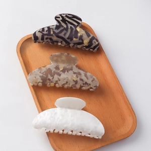 Three vintage acetate hair claws in geometric patterns and pearl white on a wooden tray