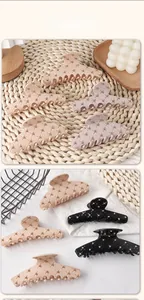 Detail showing matte acrylic hair claw clips with gold rivet accents and crisscross texture