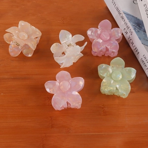 Five colorful pearlescent frangipani flower hair claws on a warm wooden background