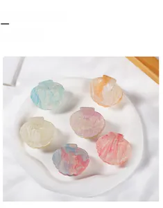 Close-up of six pearlescent shell-shaped hair claw clips with glitter in a ceramic bowl