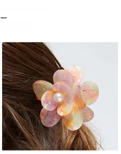 Détail d'une pince à cheveux fleur pêche avec perle sur des cheveux châtain foncé